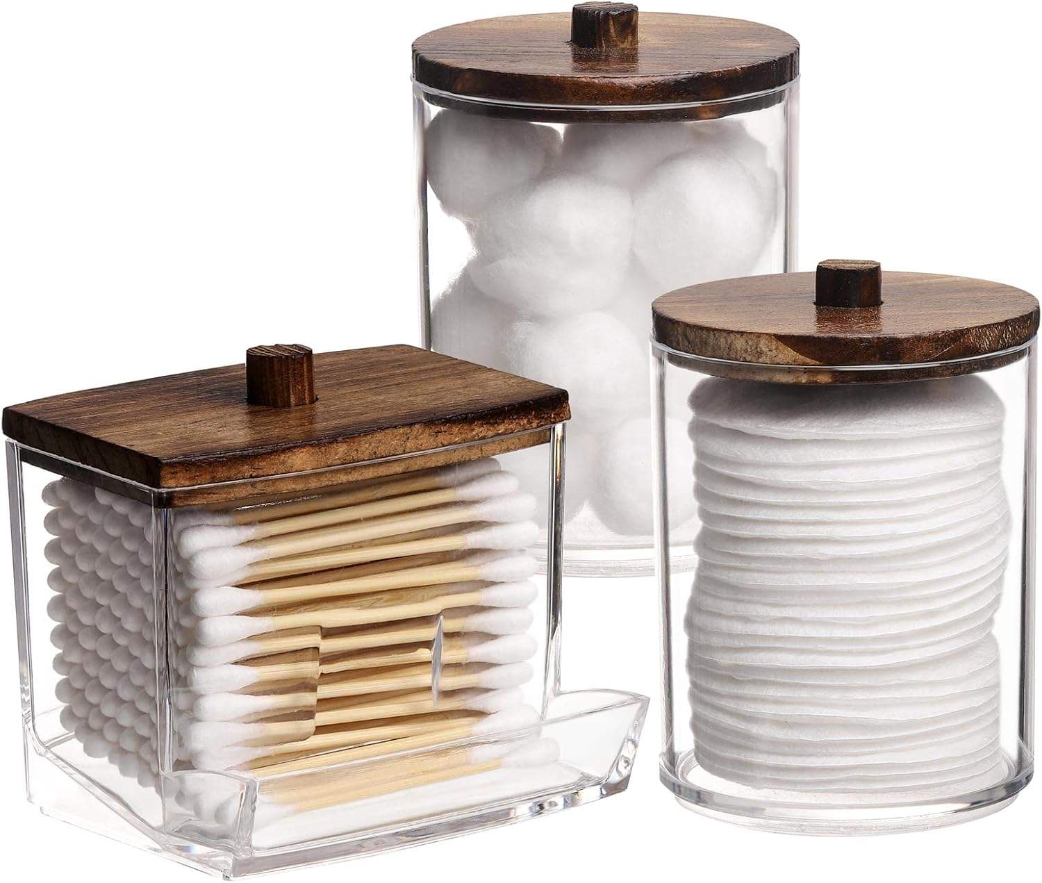 Clear bathroom apothecary jars with warm wood lids holding cotton balls, swabs, and pads on a bright neutral vanity with cozy minimalist style.