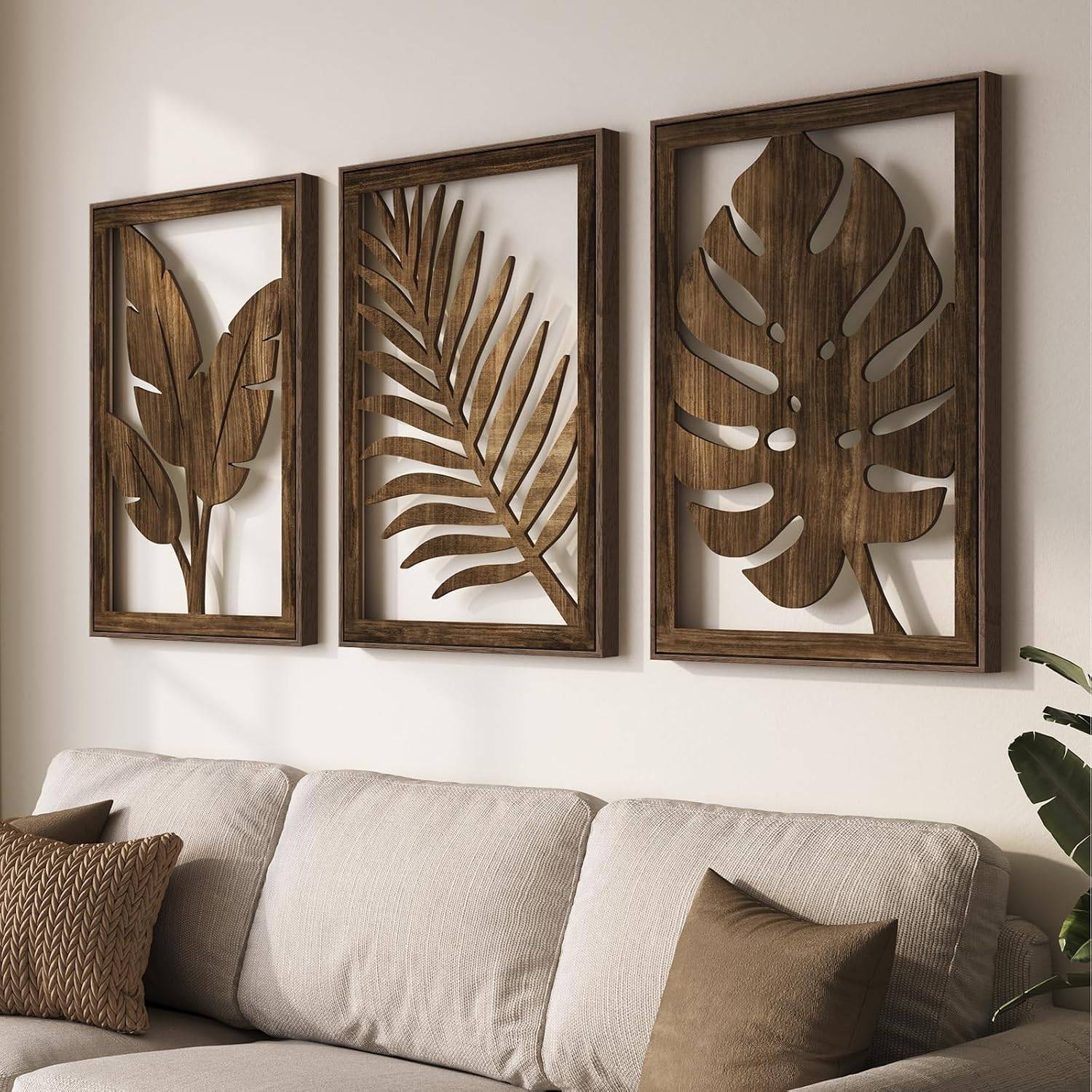 Three carved wood botanical wall art panels above a cream linen sofa with neutral pillows, warm natural light, and a potted plant for boho living room decor.