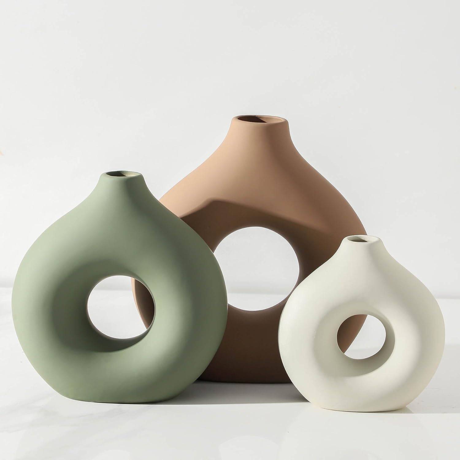 Three sculptural ceramic vases in sage green, terracotta brown, and cream styled on a bright shelf with soft neutral minimalist decor