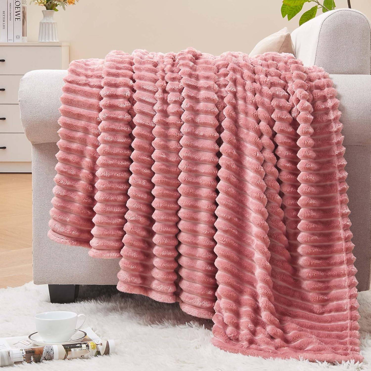 Blush pink ribbed fleece throw blanket draped over a neutral sofa with pillows, soft natural light, wood floor, plant, and calm feminine decor.