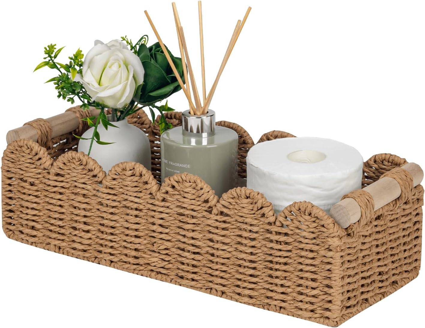 Neutral woven scalloped basket with wooden handles styled with toilet paper, reed diffuser, ceramic vase, white rose, and greenery for small bathroom basket organization.