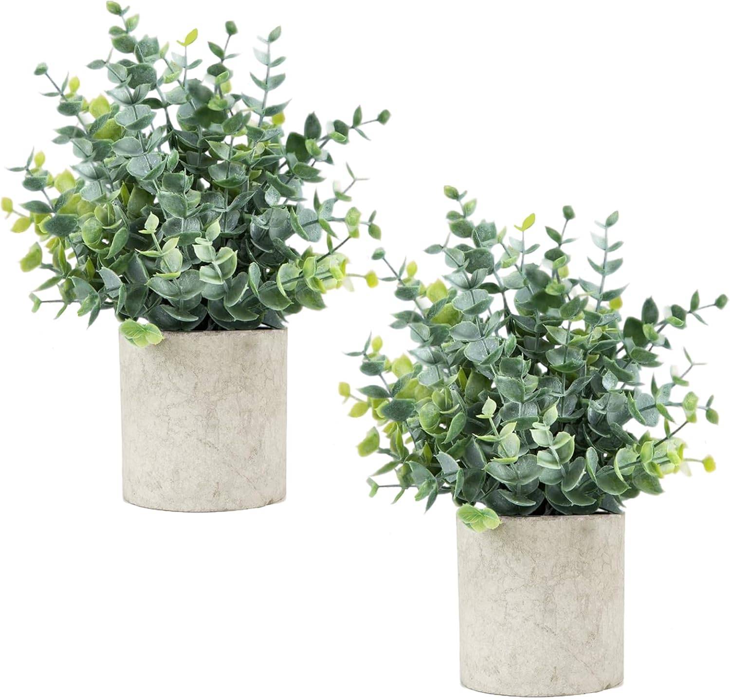 Two small sage green faux eucalyptus plants in textured stone-look pots, styled for bathroom shelf decor with a calm neutral farmhouse mood.