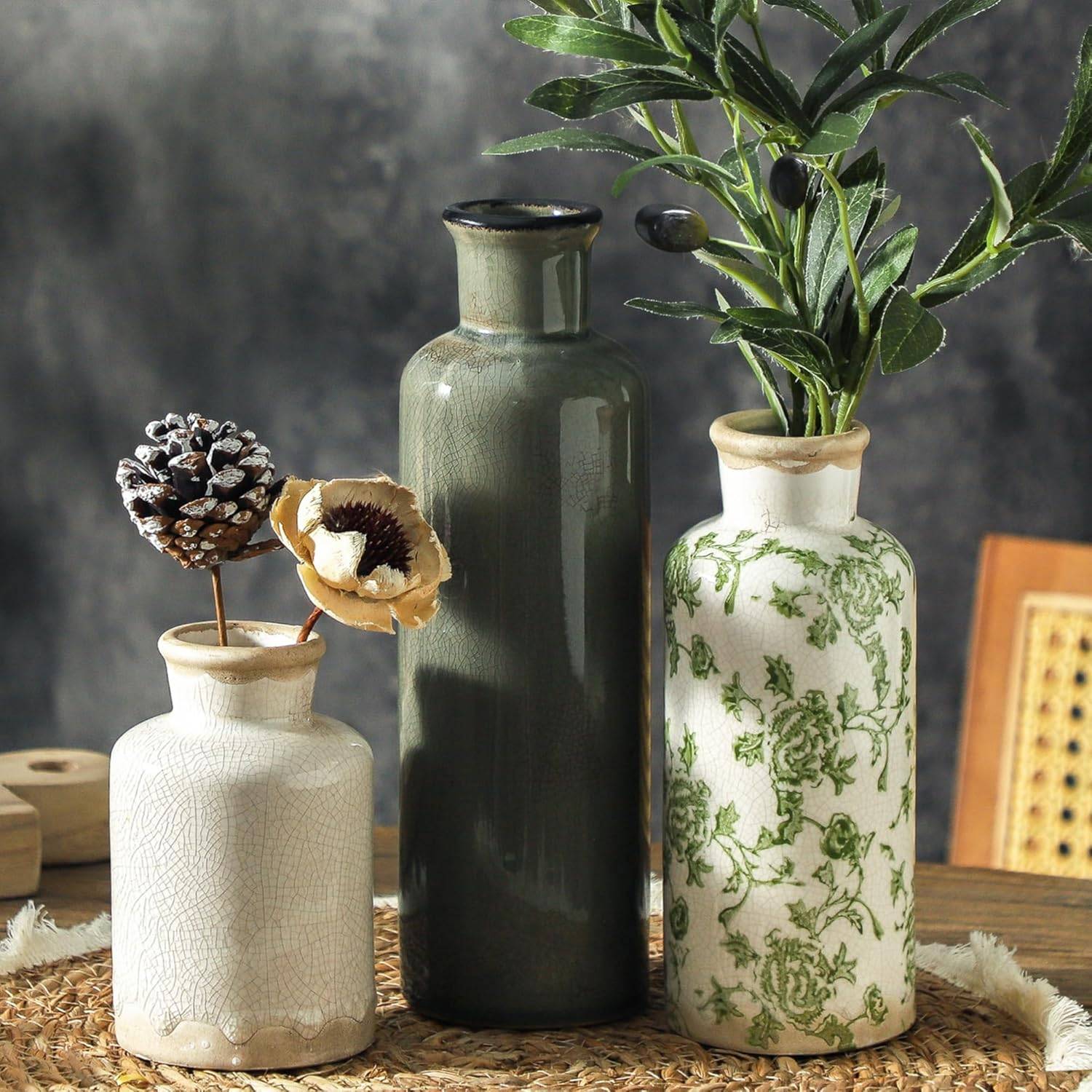 Set of three green and beige vintage ceramic vases styled with dried flowers and olive branches on a woven tray in warm rustic decor.