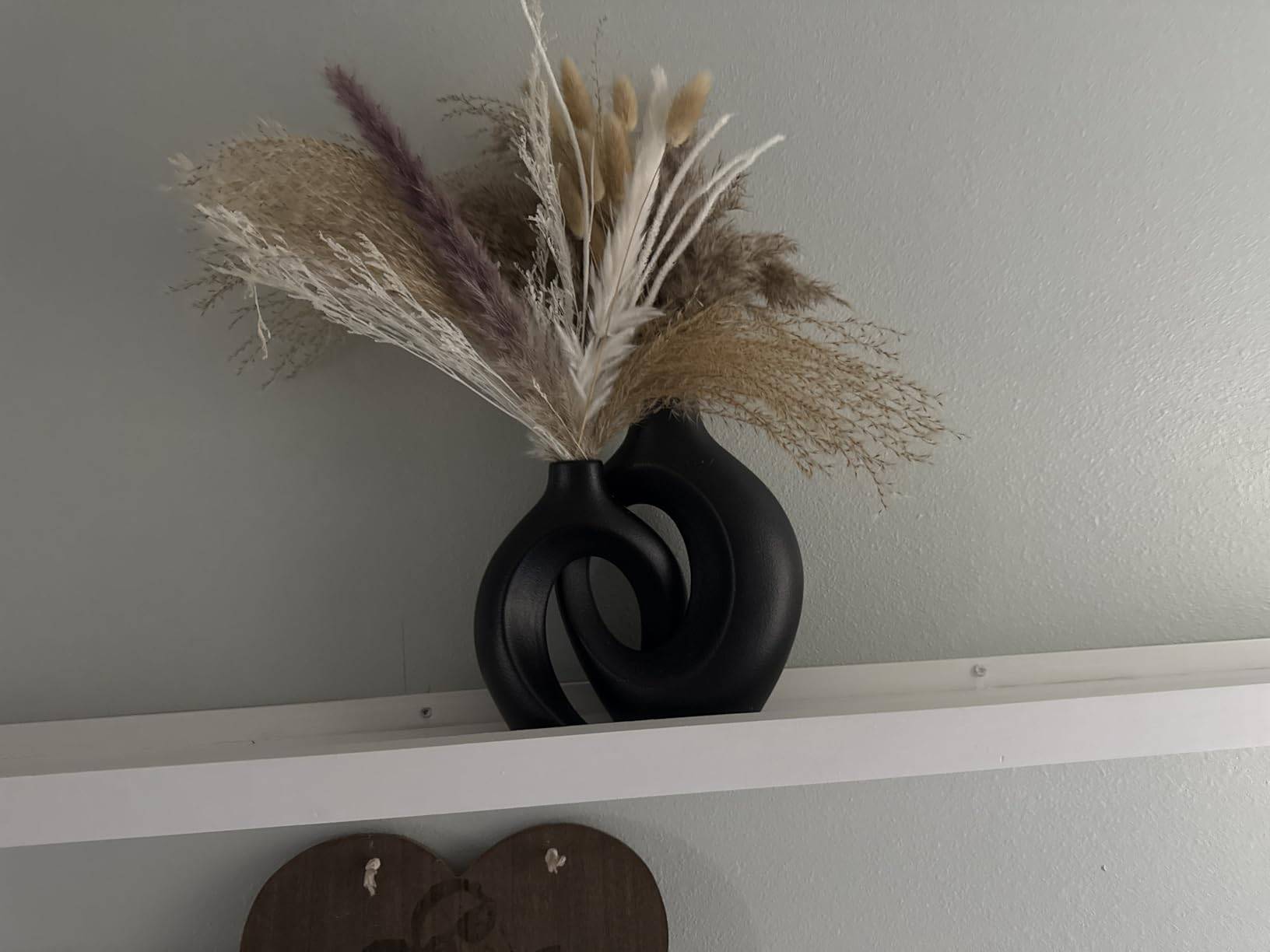 Black hollow ceramic round vases with dried pampas grass on a white shelf against a textured neutral wall, warm minimalist boho decor