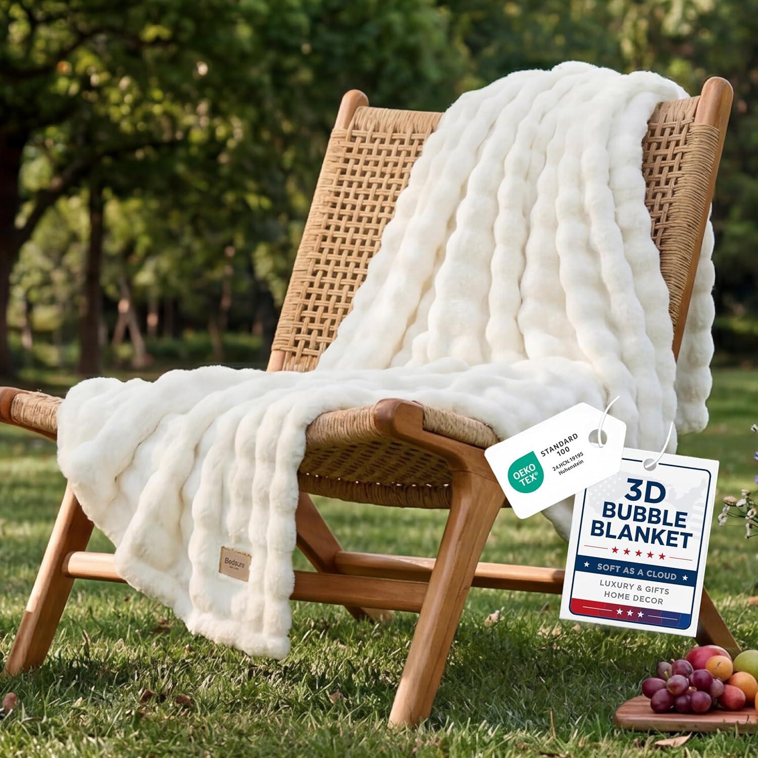 Off white bubble fleece throw blanket draped over a woven lounge chair in bright natural light, styled with warm wood tones and cozy neutral decor.