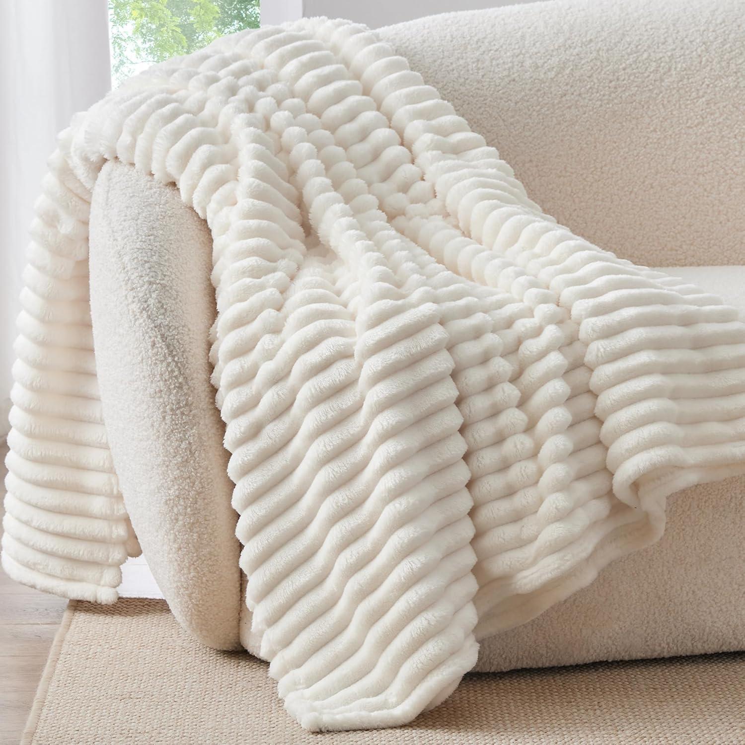 Cream white ribbed fleece throw blanket draped over a boucle couch in bright natural light, styled for soft neutral living room decor.