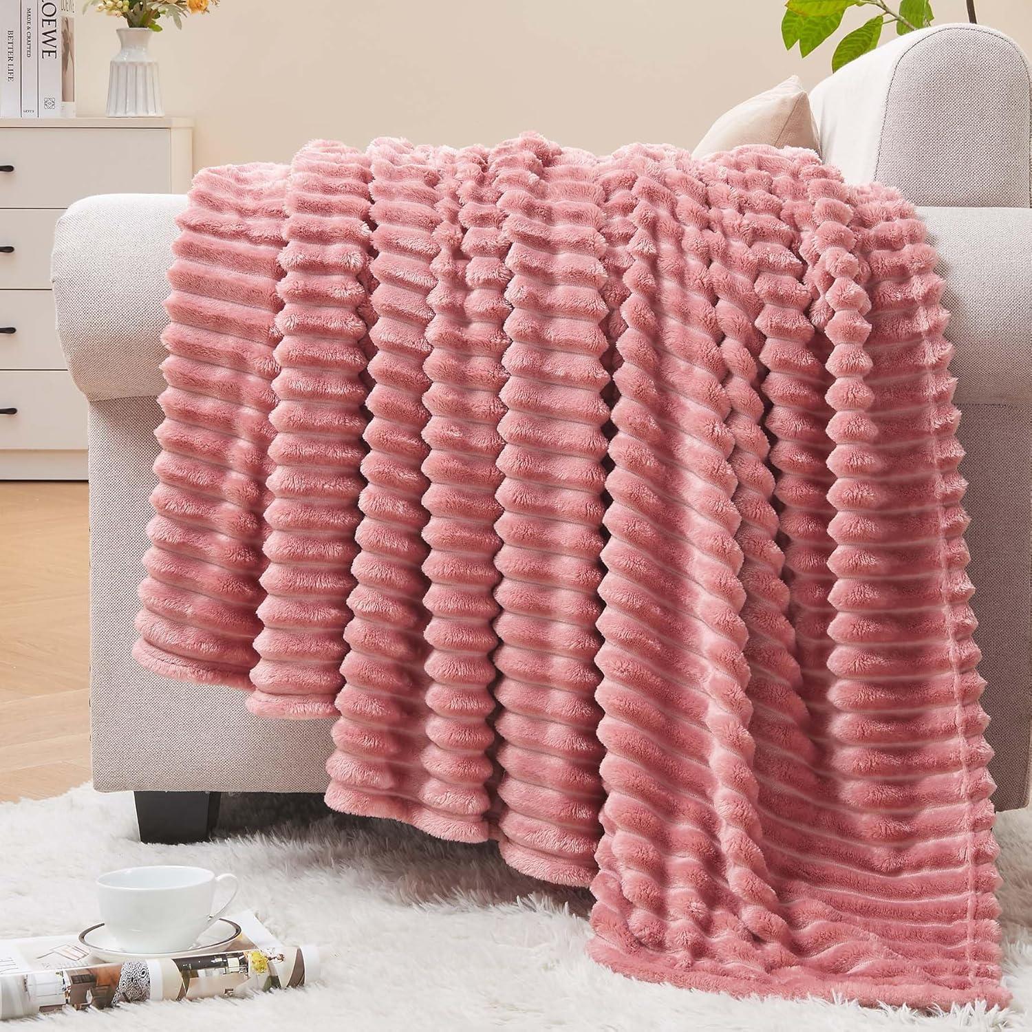 Blush pink ribbed fleece throw blanket draped over a neutral sofa with pillows, soft natural light, wood floor, plant, and calm feminine decor.