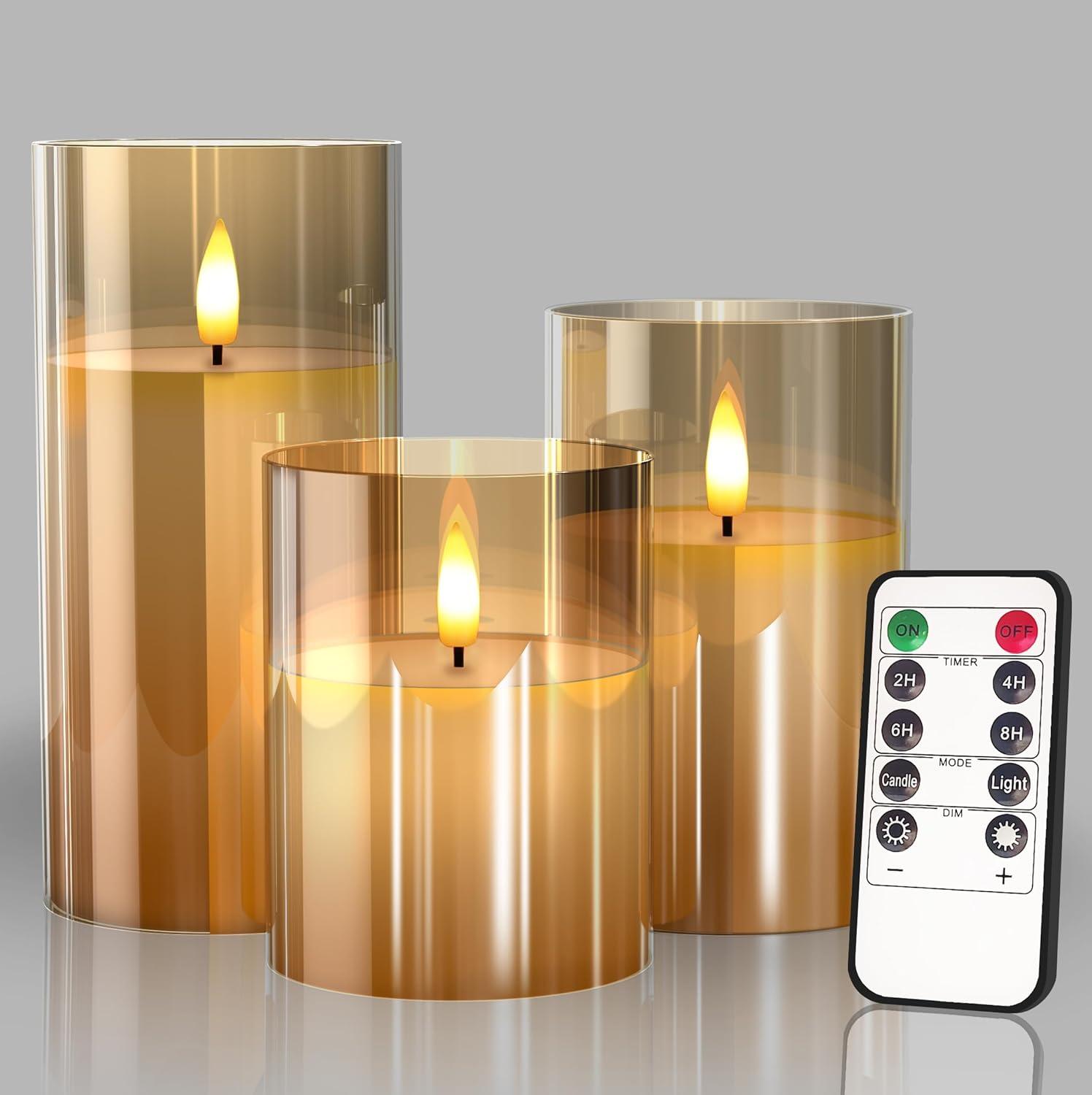 Three gold glass flameless pillar candles with warm flickering LED flames and a remote, styled as elegant neutral home lighting.