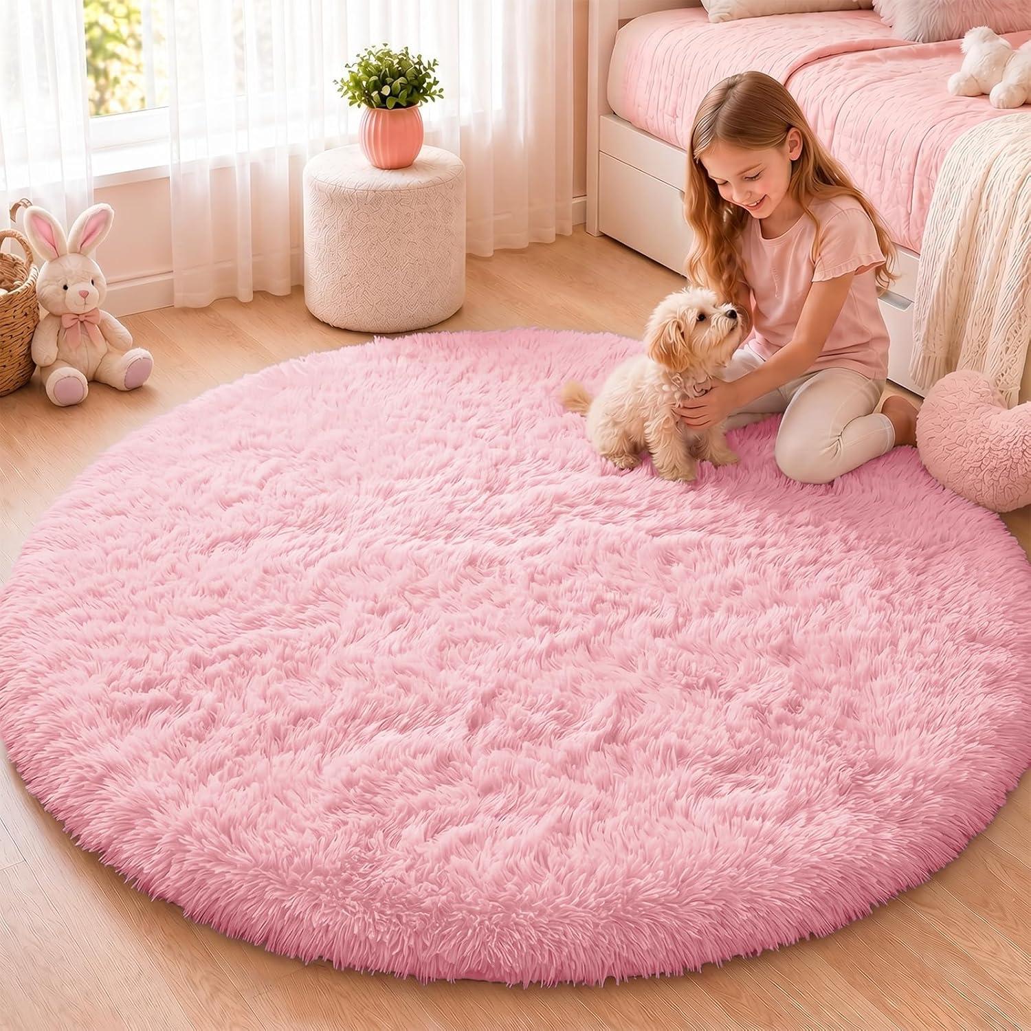 Soft pink round shag rug in a bright bedroom with pale wood floors, blush bedding, sheer curtains, plush pillows, and cozy feminine decor.