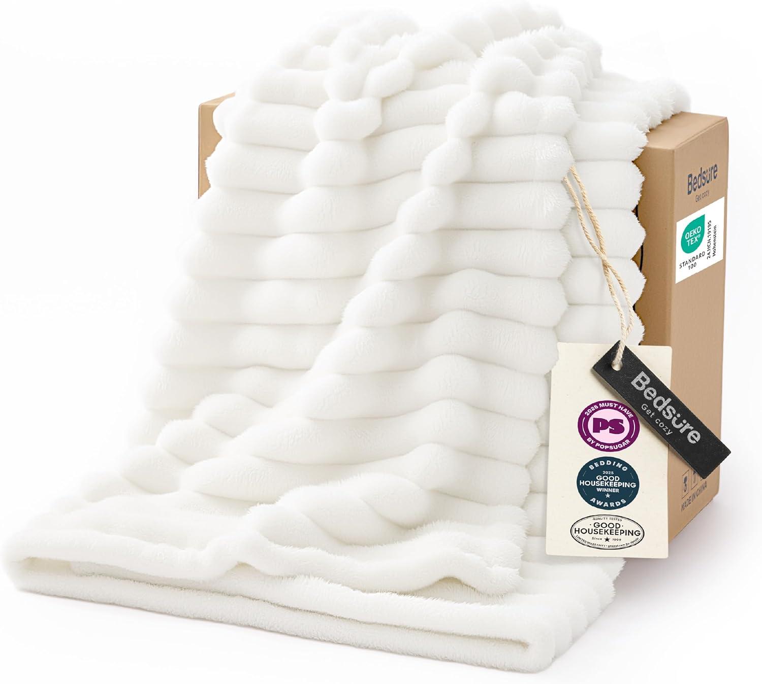 Off-white textured fleece white throw blanket draped from a cardboard gift box on a bright white background, showing plush wavy ridges and soft sofa-ready texture.