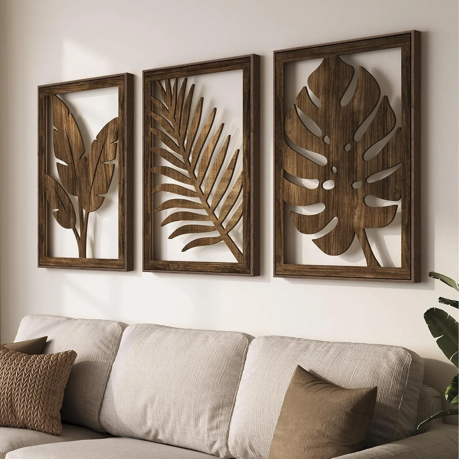 Three carved wood botanical wall art panels above a cream linen sofa with neutral pillows, warm natural light, and a potted plant for boho living room decor.