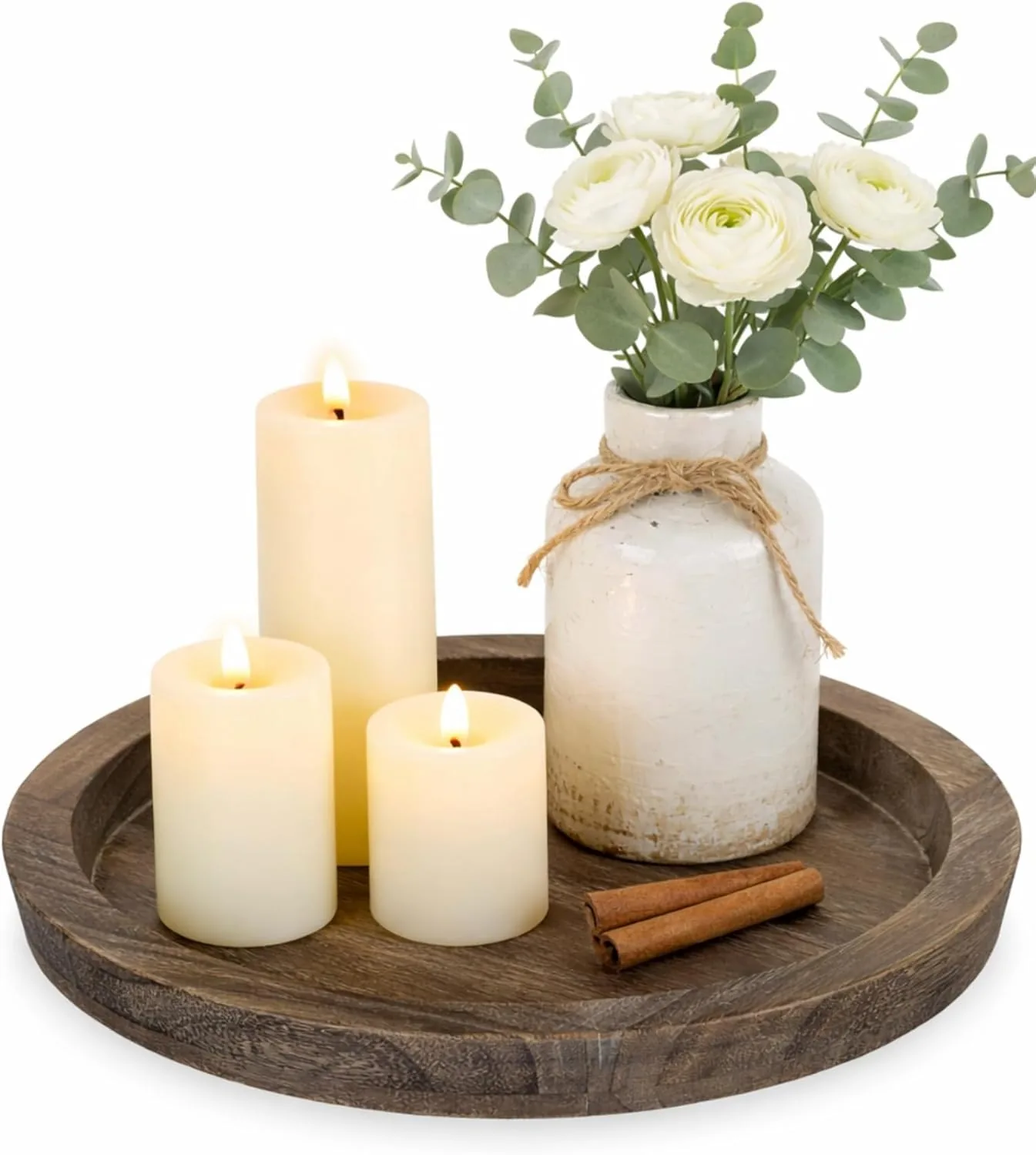 Round distressed wood tray styled with glowing pillar candles, a rustic ceramic vase, white flowers, eucalyptus, and cinnamon sticks for a farmhouse coffee table decor tray.