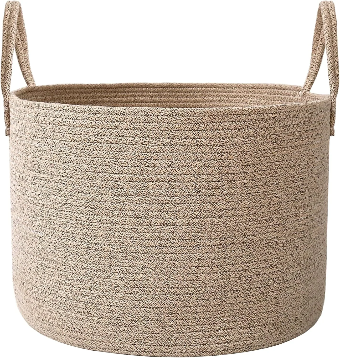Large oatmeal woven rope basket with handles styled beside a neutral sofa, filled with soft blankets and pillows in a bright warm living room.