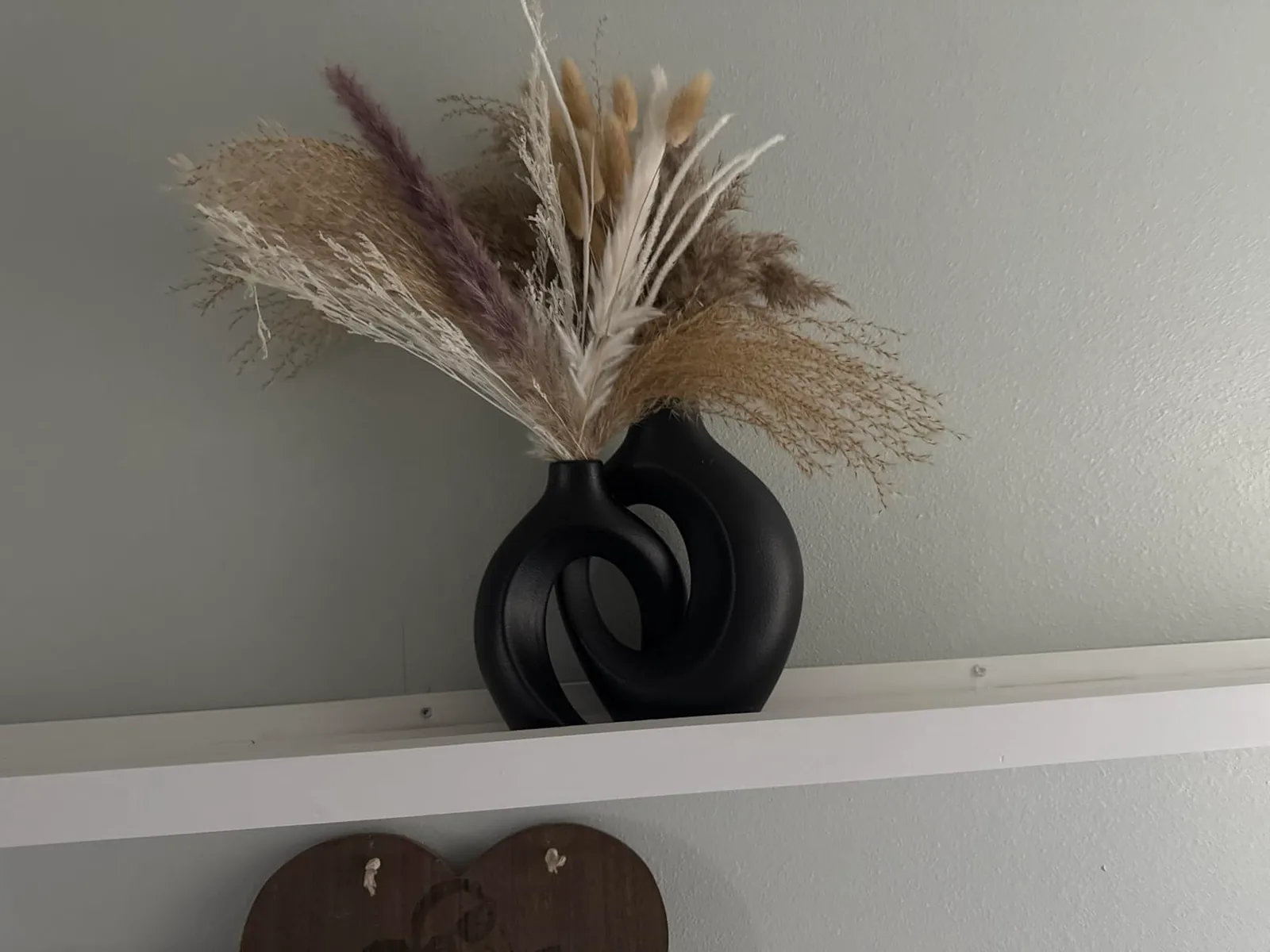 Black hollow ceramic round vases with dried pampas grass on a white shelf against a textured neutral wall, warm minimalist boho decor